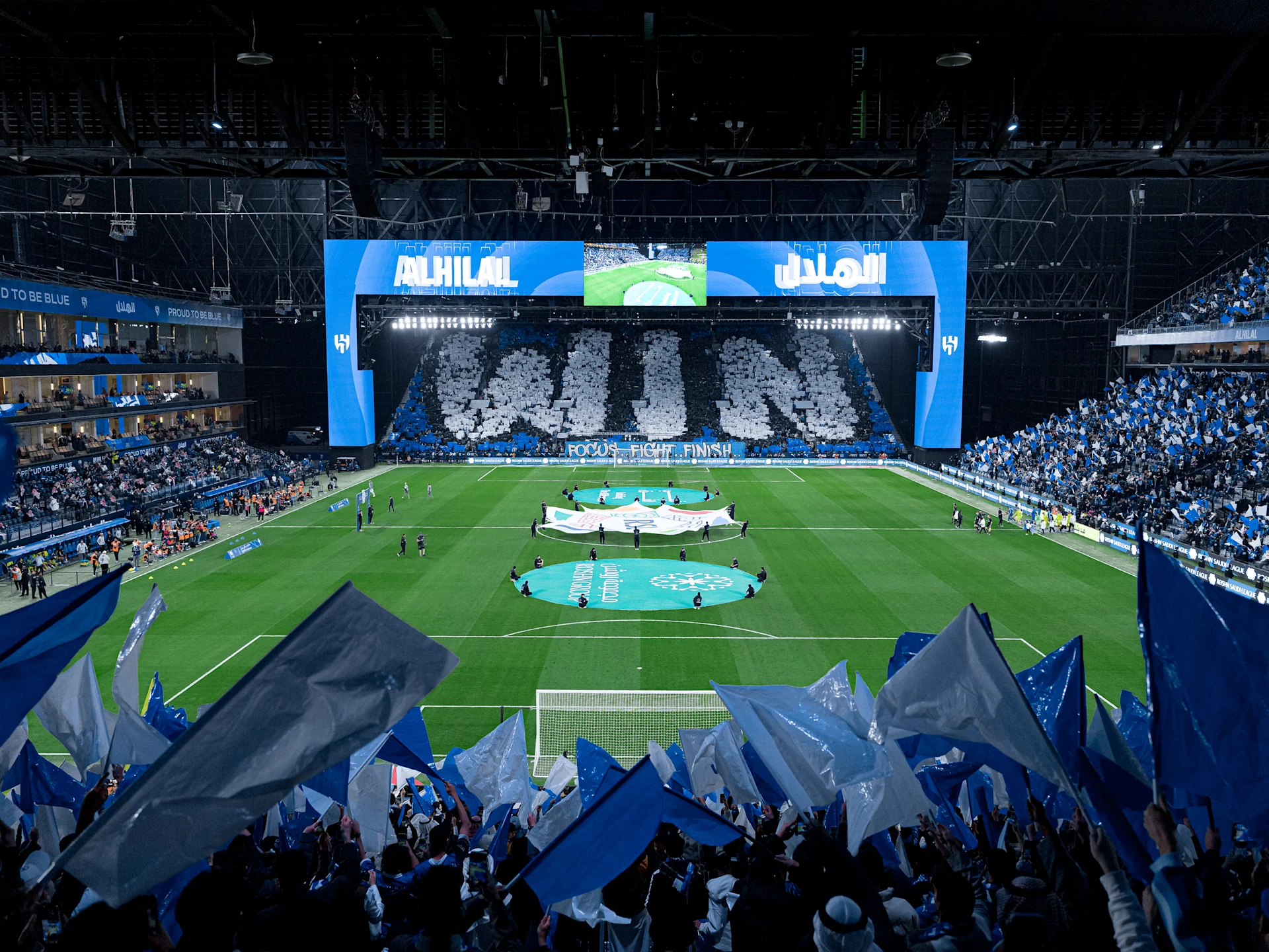 Kingdom Arena at night, filled with Al-Hilal supporters waving blue flags